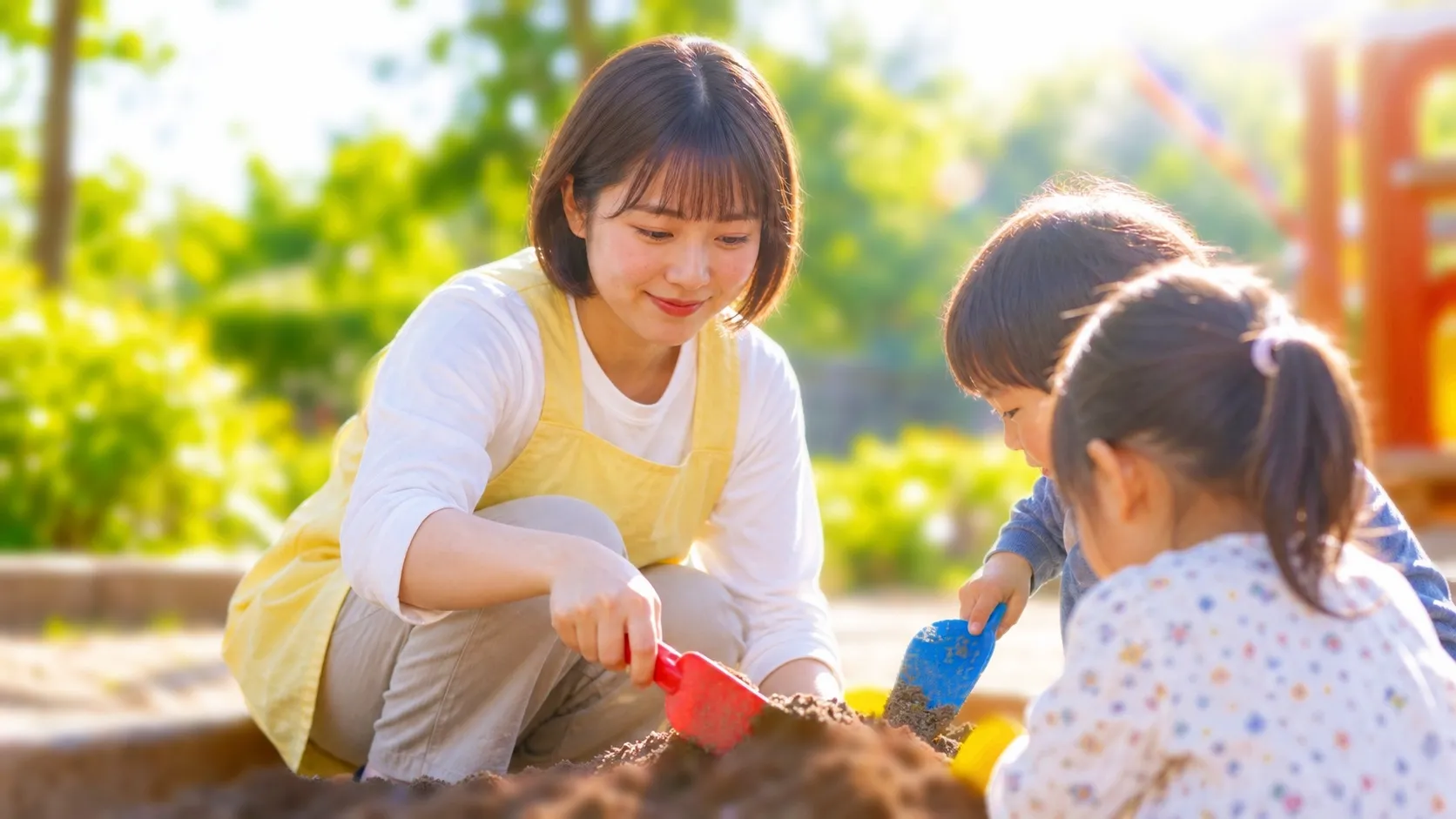 園庭の砂場で子どもたちと遊ぶ保育士